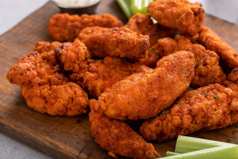 Buffalo chicken strips on a board with ranch and celery